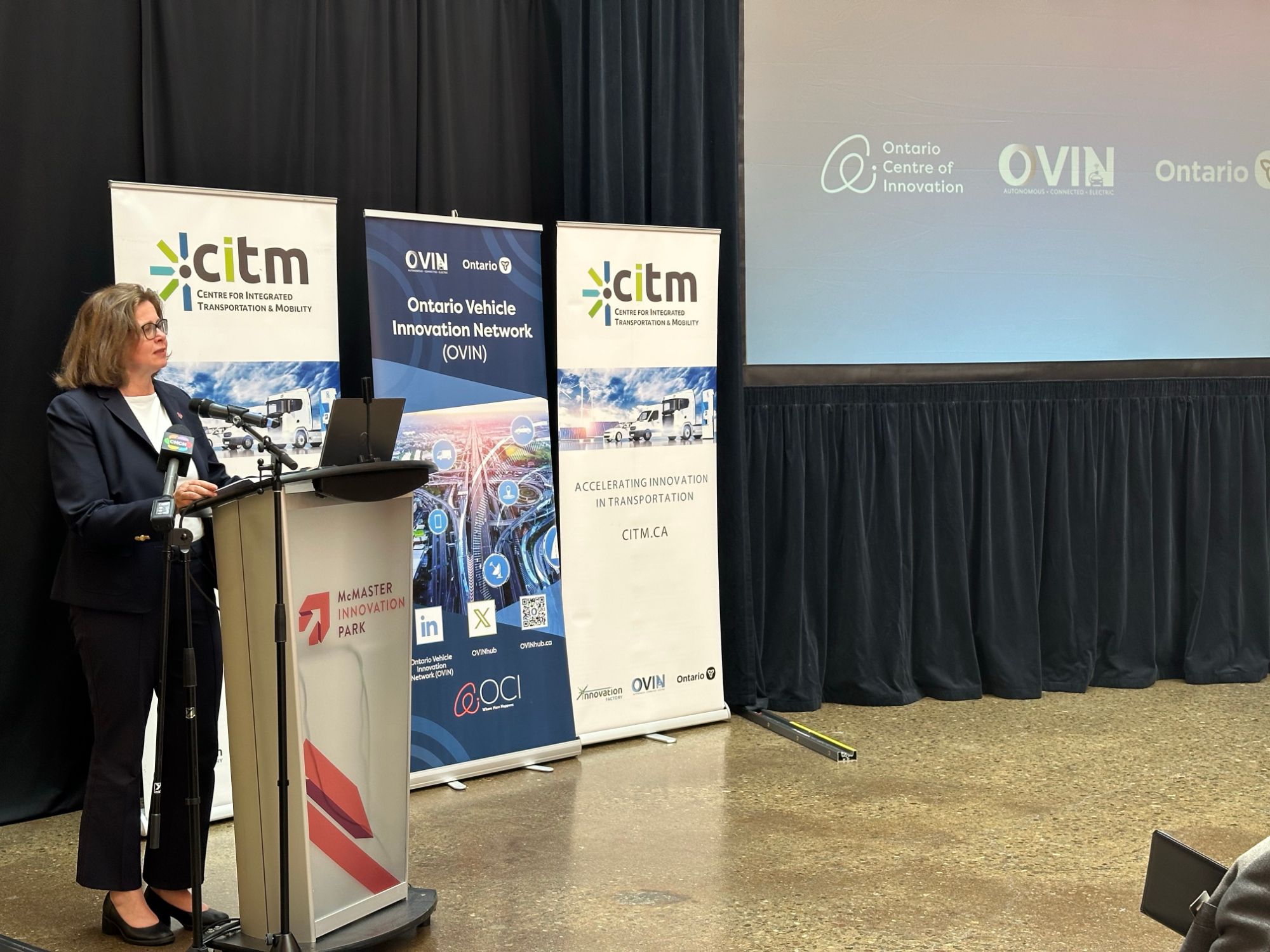 Speaker addressing attendees at the OVIN funding announcement event, with Ontario Centre of Innovation and OVIN signage on screen